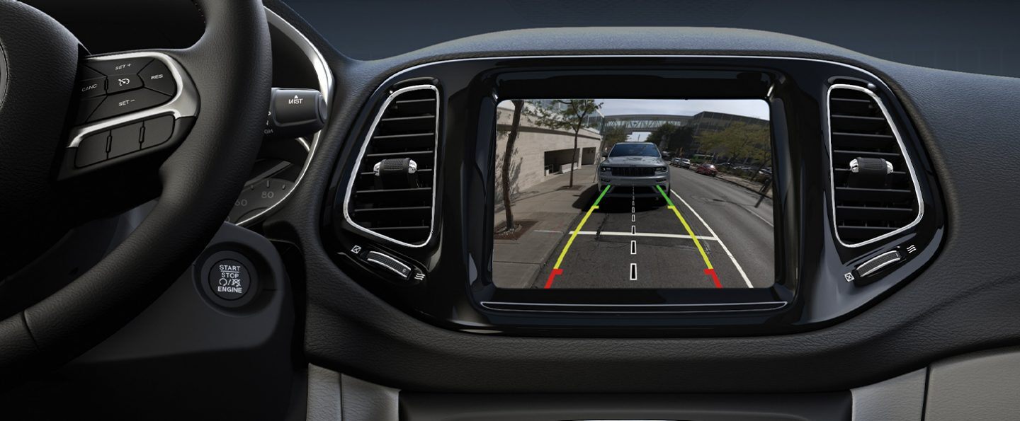A close-up of the touchscreen in the 2021 Jeep Compass displaying the view from the rear camera with gridlines indicating the trajectory of the vehicle.