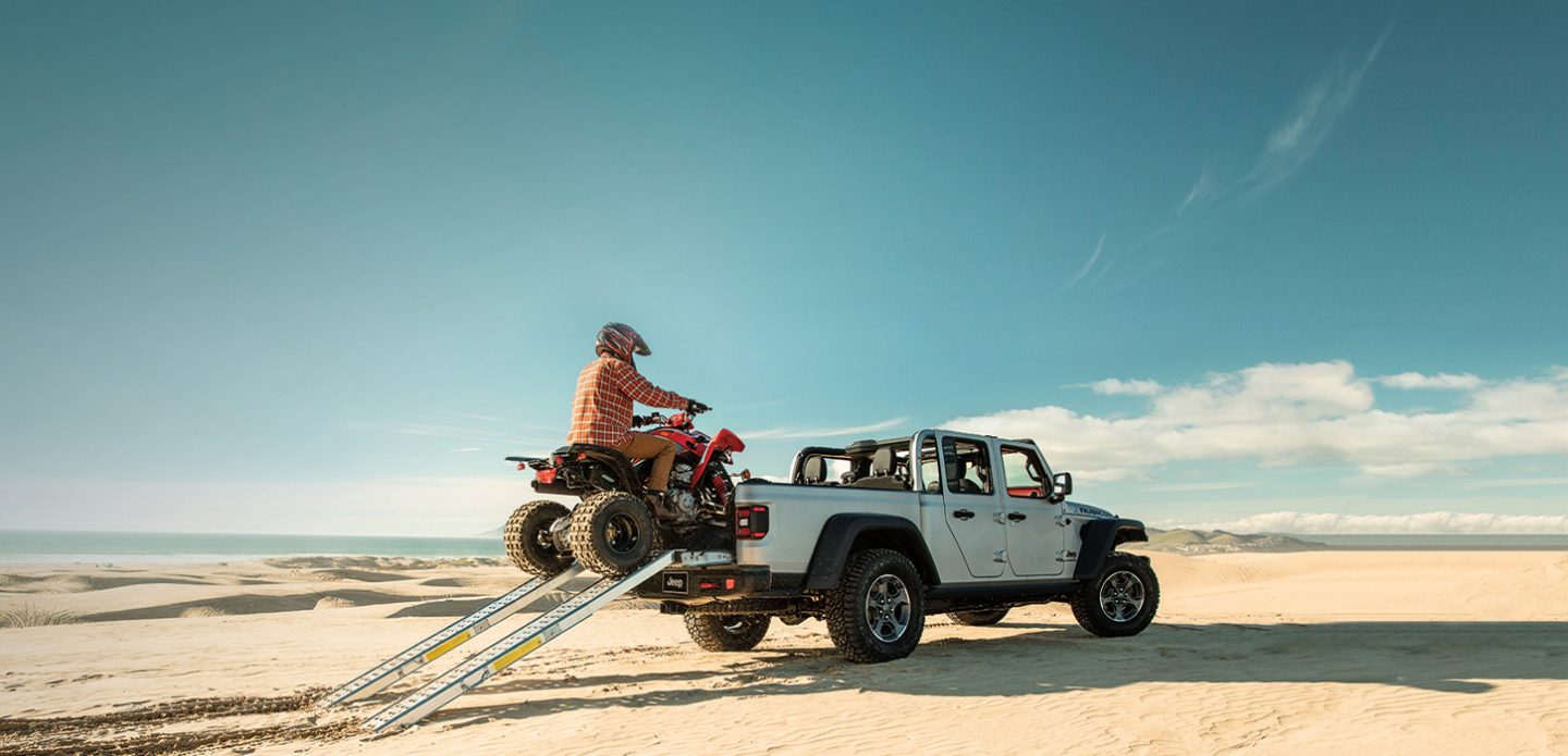 A man driving an ATV up a ramp into the bed of a 2021 Jeep Gladiator Rubicon.