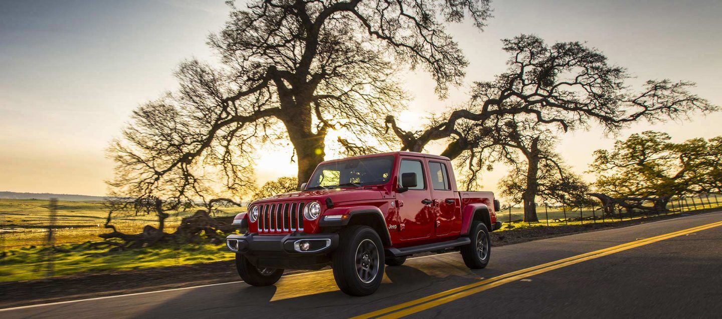 A 2021 Jeep Gladiator Overland being driven on a highway near grassy fields at sunset.
