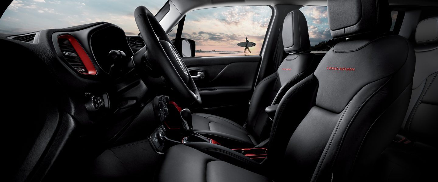 Side interior view of the front seats on the 2021 Jeep Renegade Trailhawk, as a surfer walks on the beach in the background.